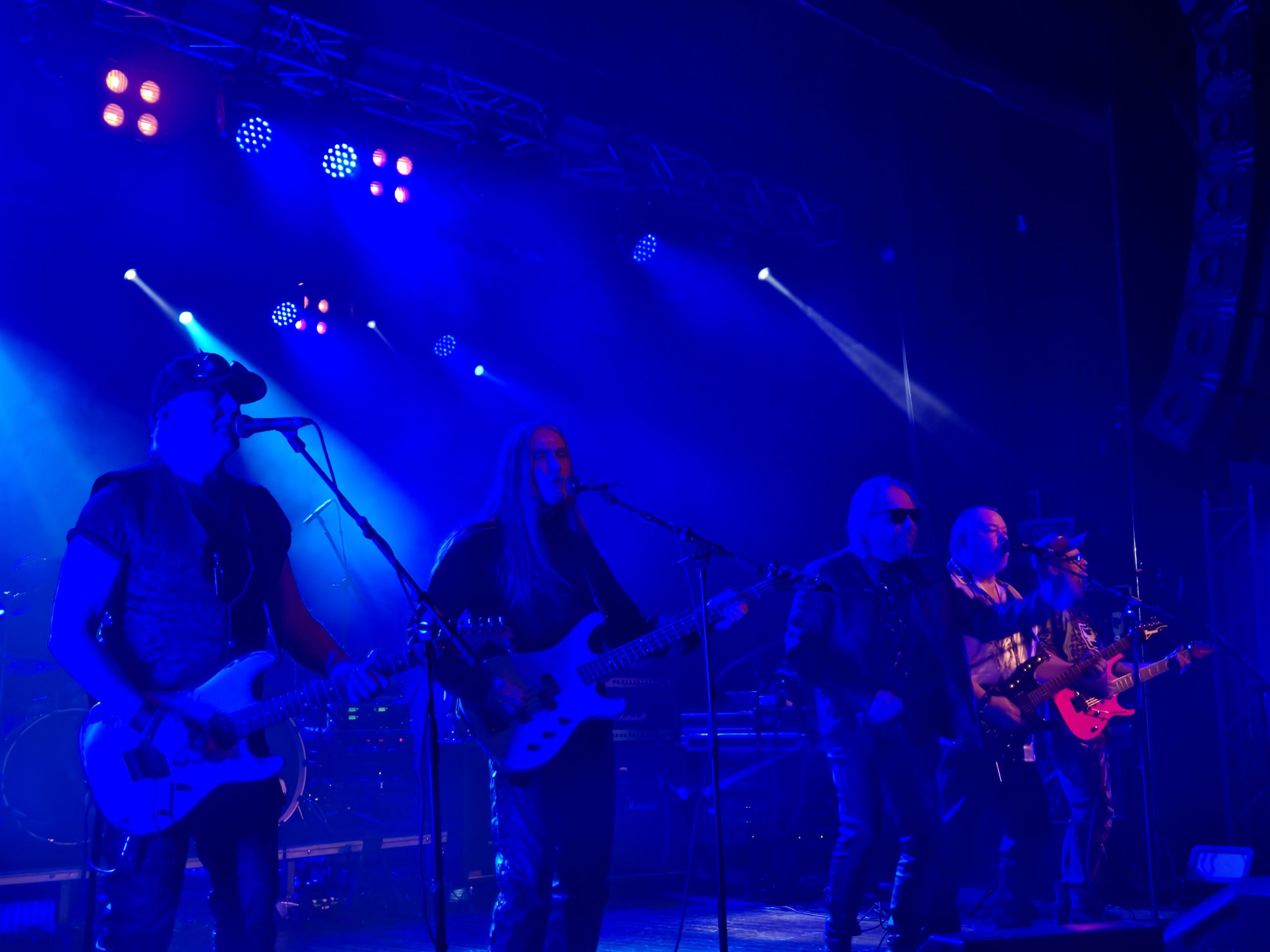 Bandet Quest. Fem män varav tre gitarrister, två elbasister och en frontfigur med solglasögon. Instrumentalisterna sjunger i mikrofonerna.