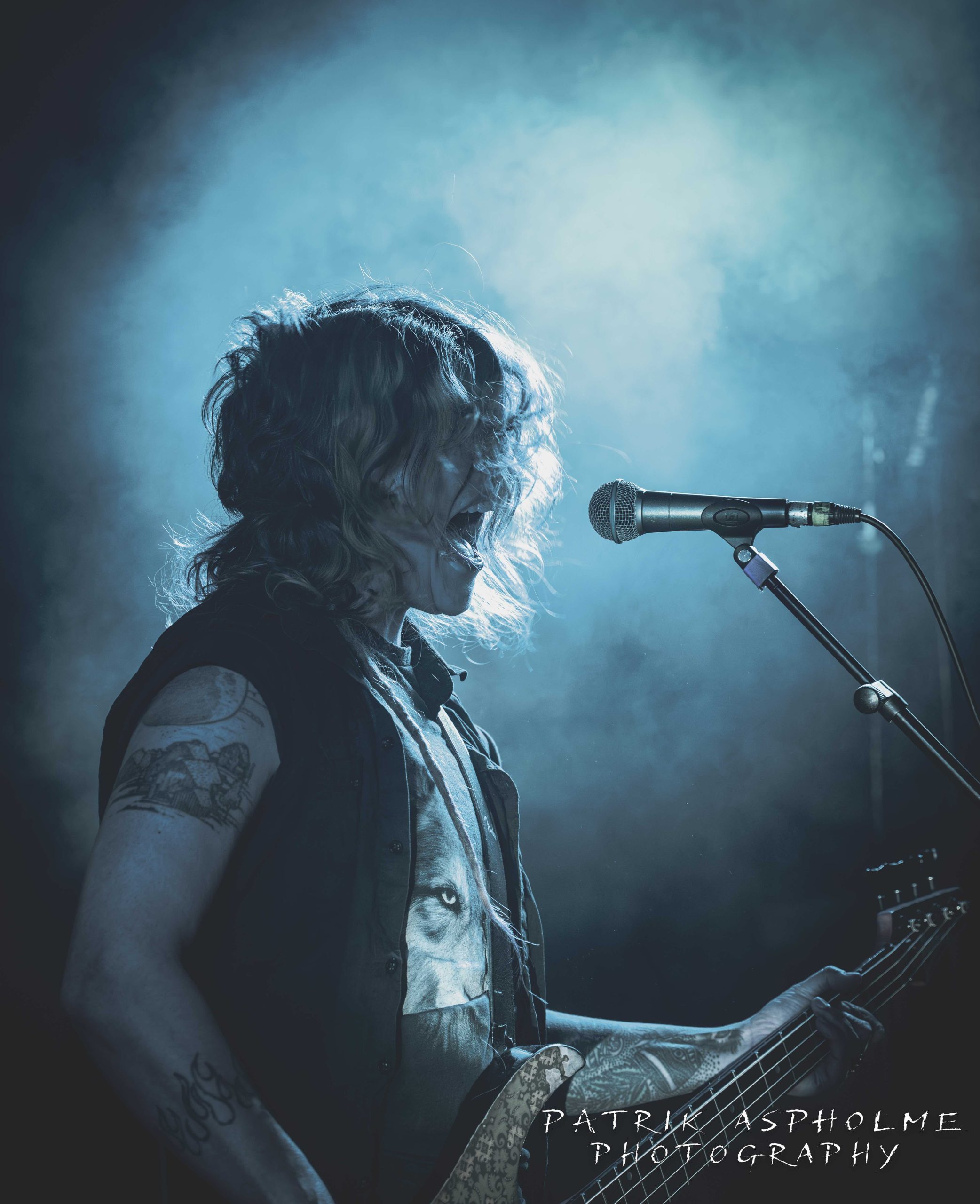 The Sensitives frontfigur spelar bas och skriker i mikrofonen i blått scenljus och rök. Hennes gröna hår täcker ansiktet.