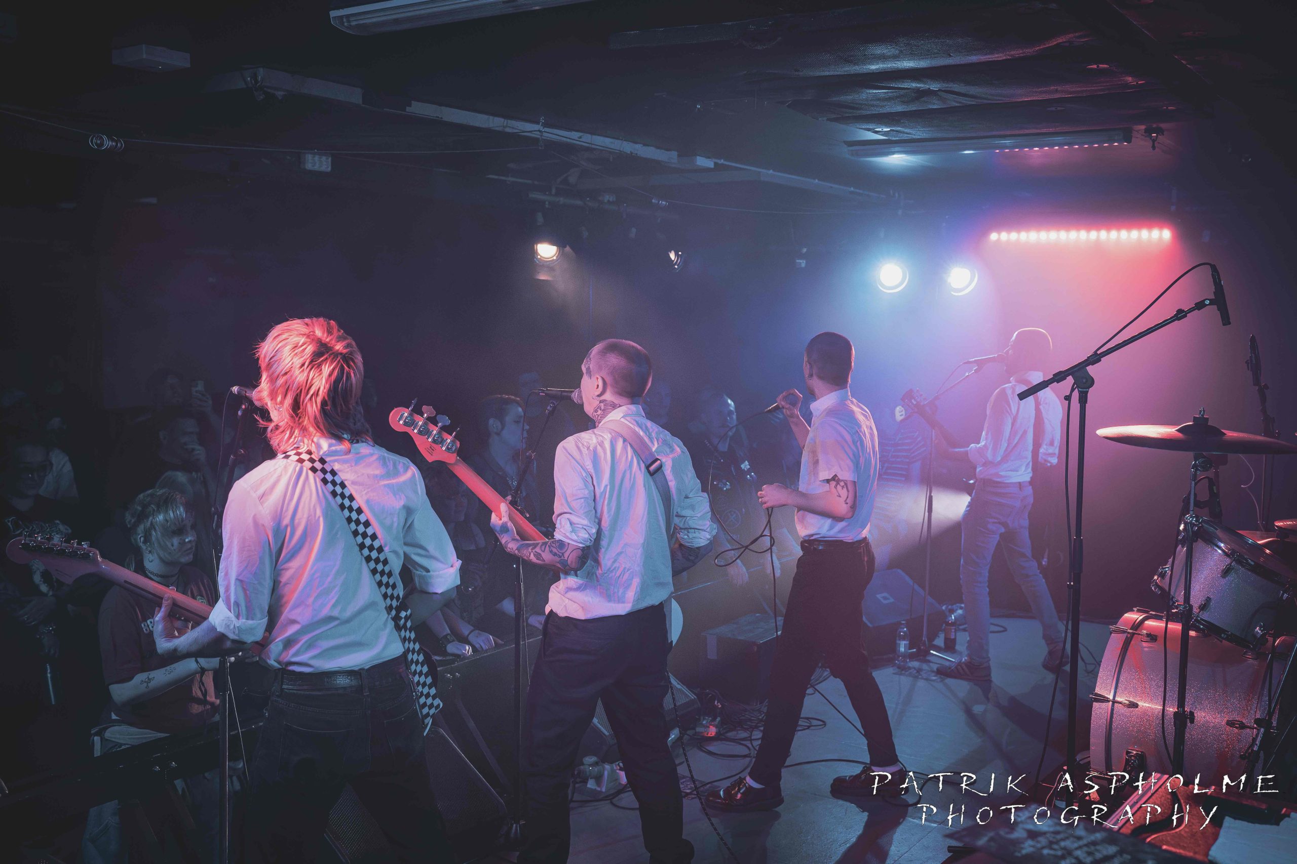 Strikt på scenen bakifrån. De står uppradade med sina respektive instrument. Alla har vita skjortor.