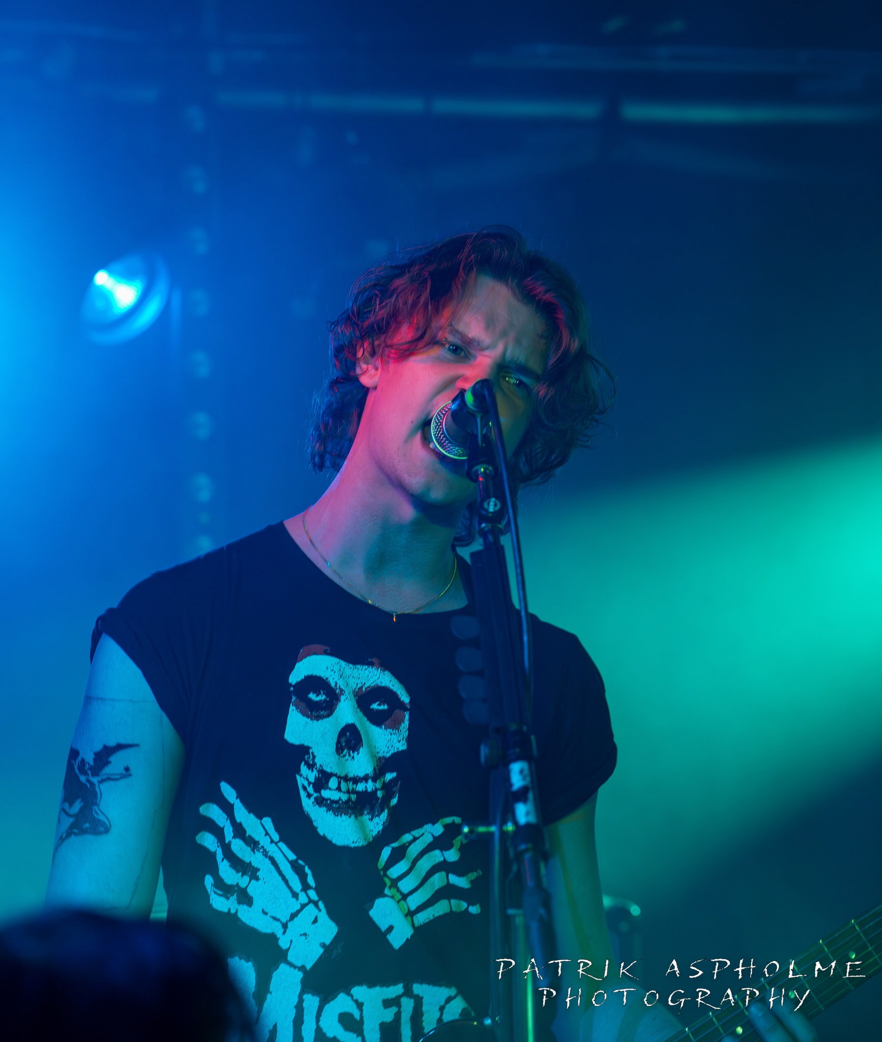 Riskbrukarnas gitarrist ser argt ut över publiken och sjunger i mikrofonen. Han har en svart Misfits-tshirt.