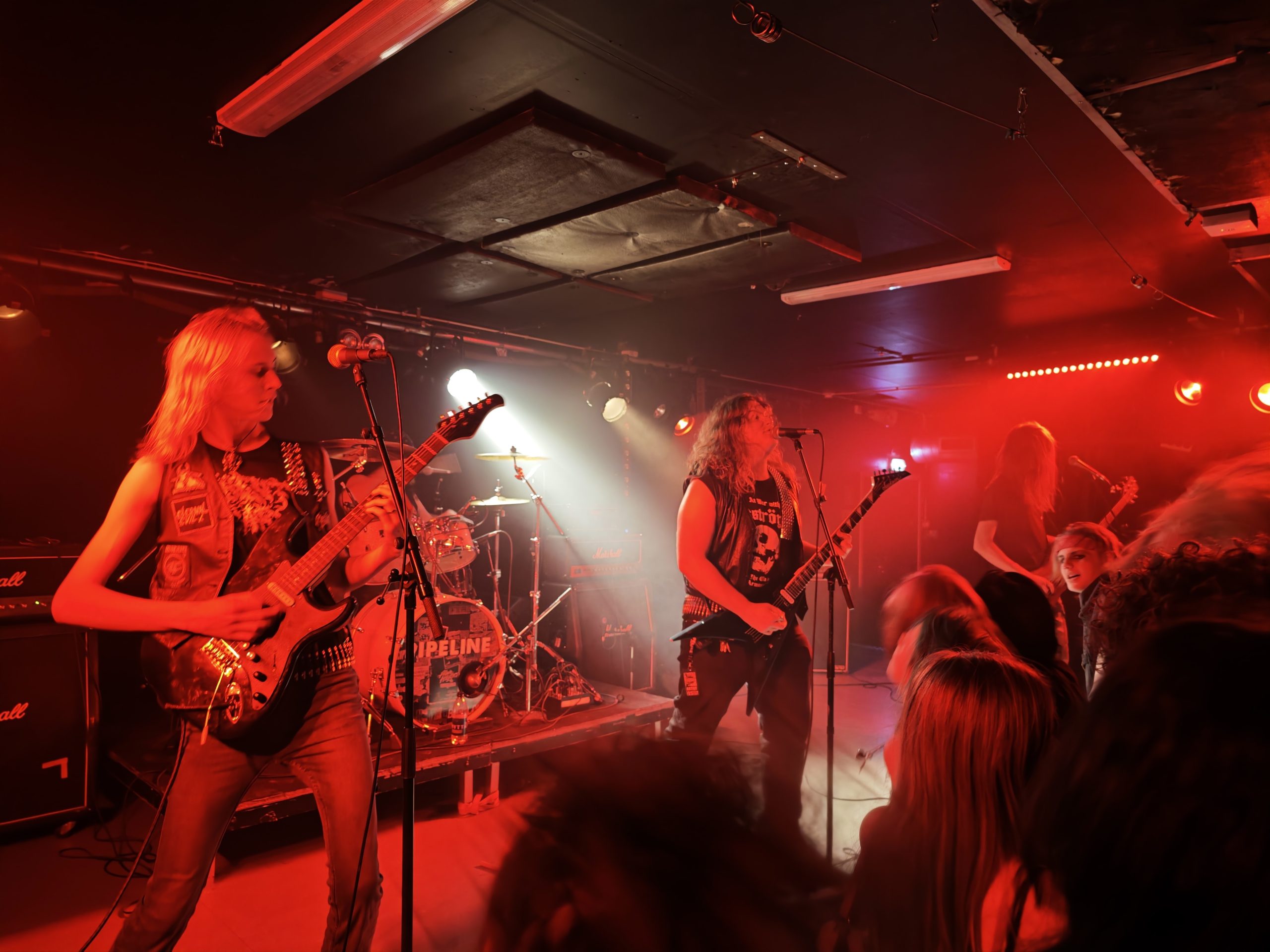 En scen i röd belysning med 4 bandmedlemmar som står och rockar