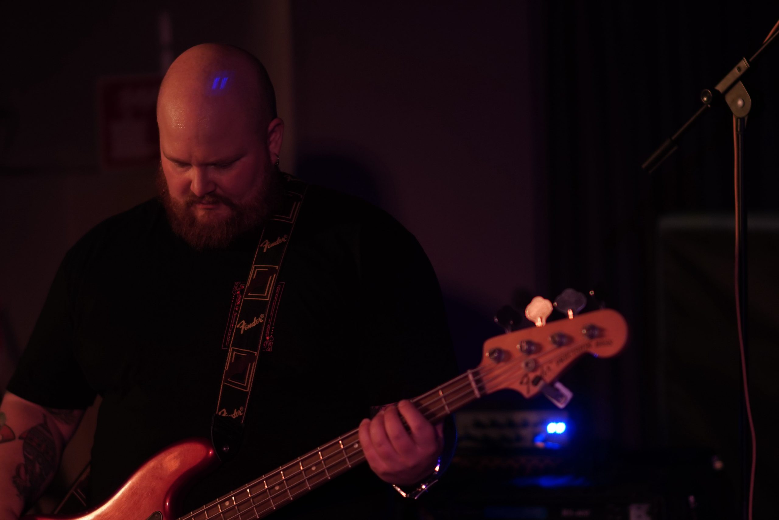 I Am Lows basist spelar på sin bas med blicken ner mot golvet. Han är skallig och har stort, rött skägg och tatuerade armar.
