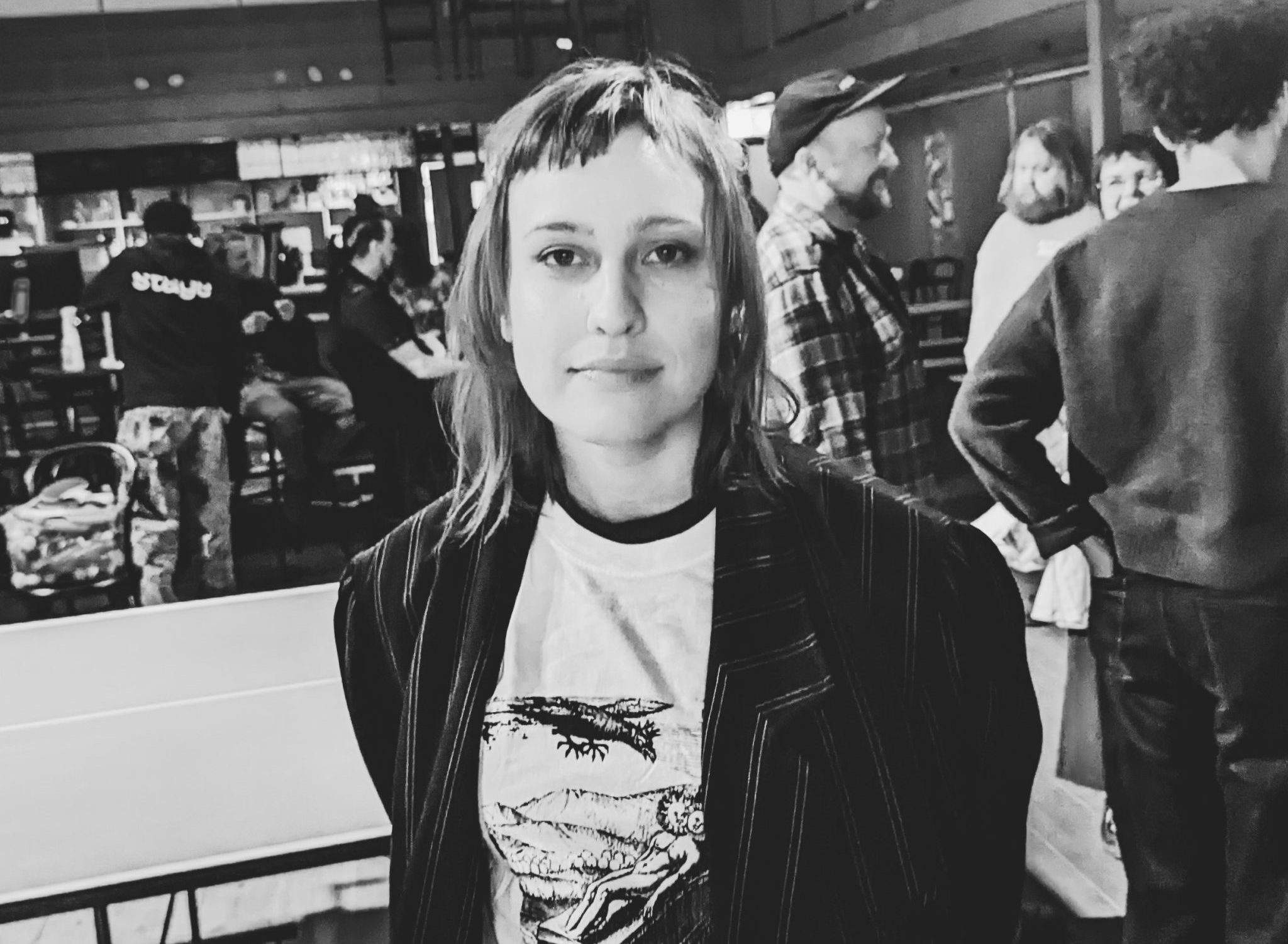 Arrangören Emelie Rehn ler in i kameran. Hon har kort lugg, en oversize jacka och står framför ett gäng besökare på Stage.