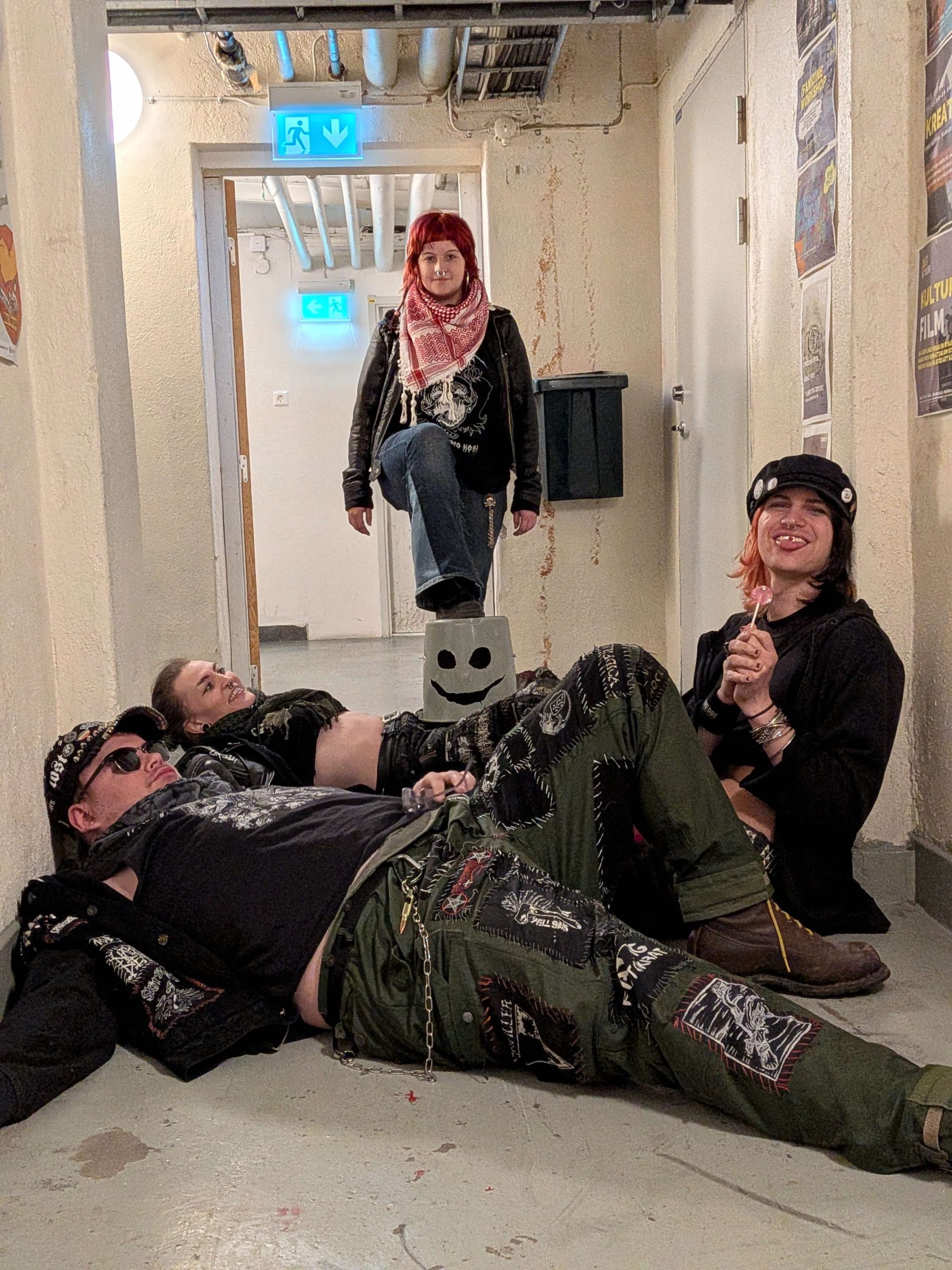 Två av bandmedlemmarna ligger ner på golvet i ett källarutrymme medan de andra två ler mot kameran.
