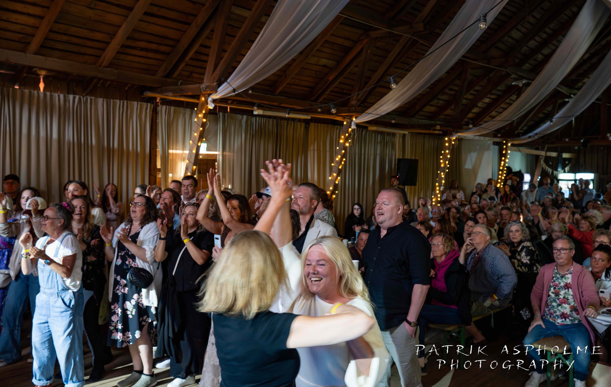 Publikbild fotat snett framifrån. Publiken klappar, dansar och är glada.