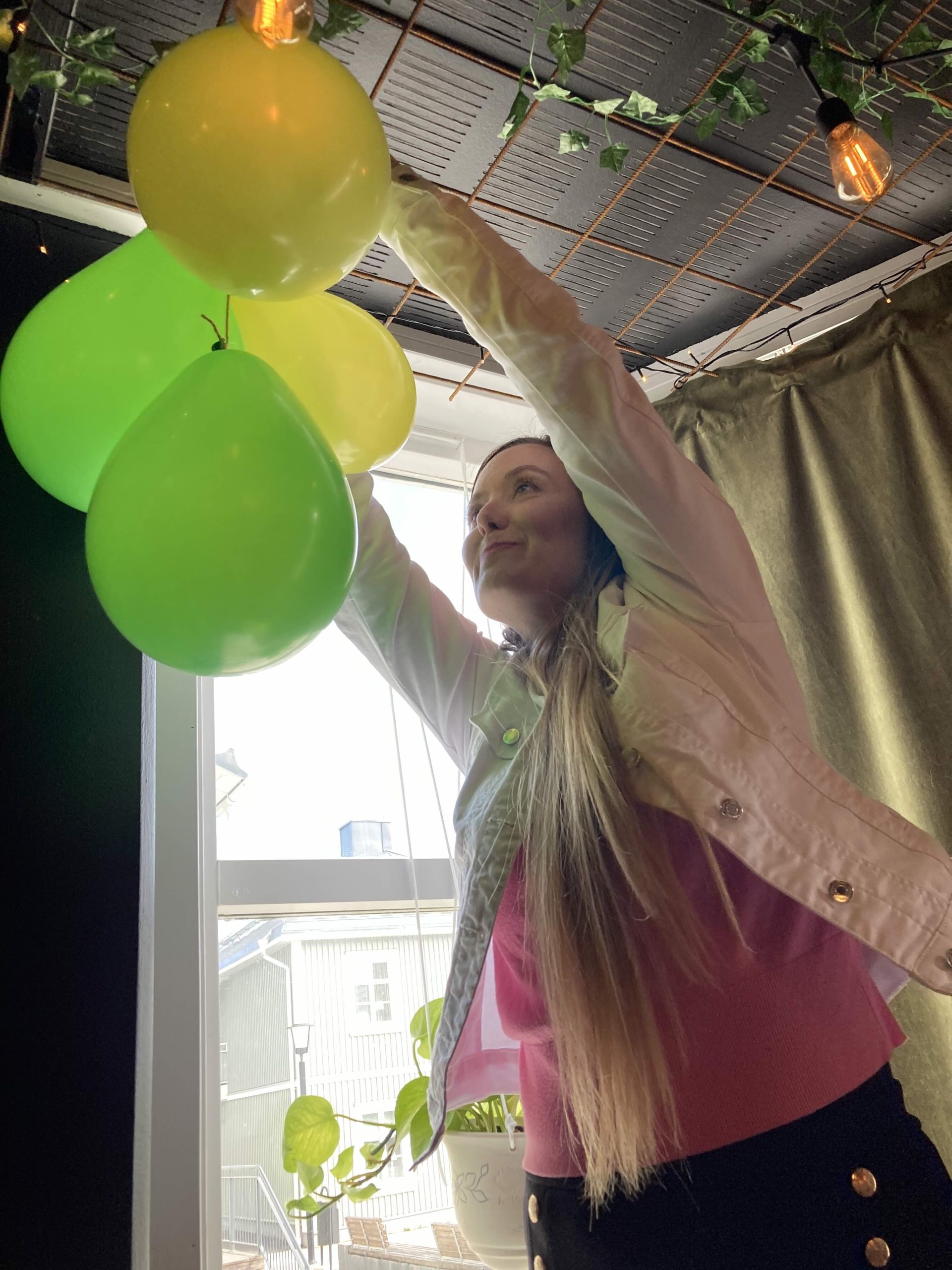 Kvinna med långt hår som hänger upp gula och grön ballonger i en klase i taket.