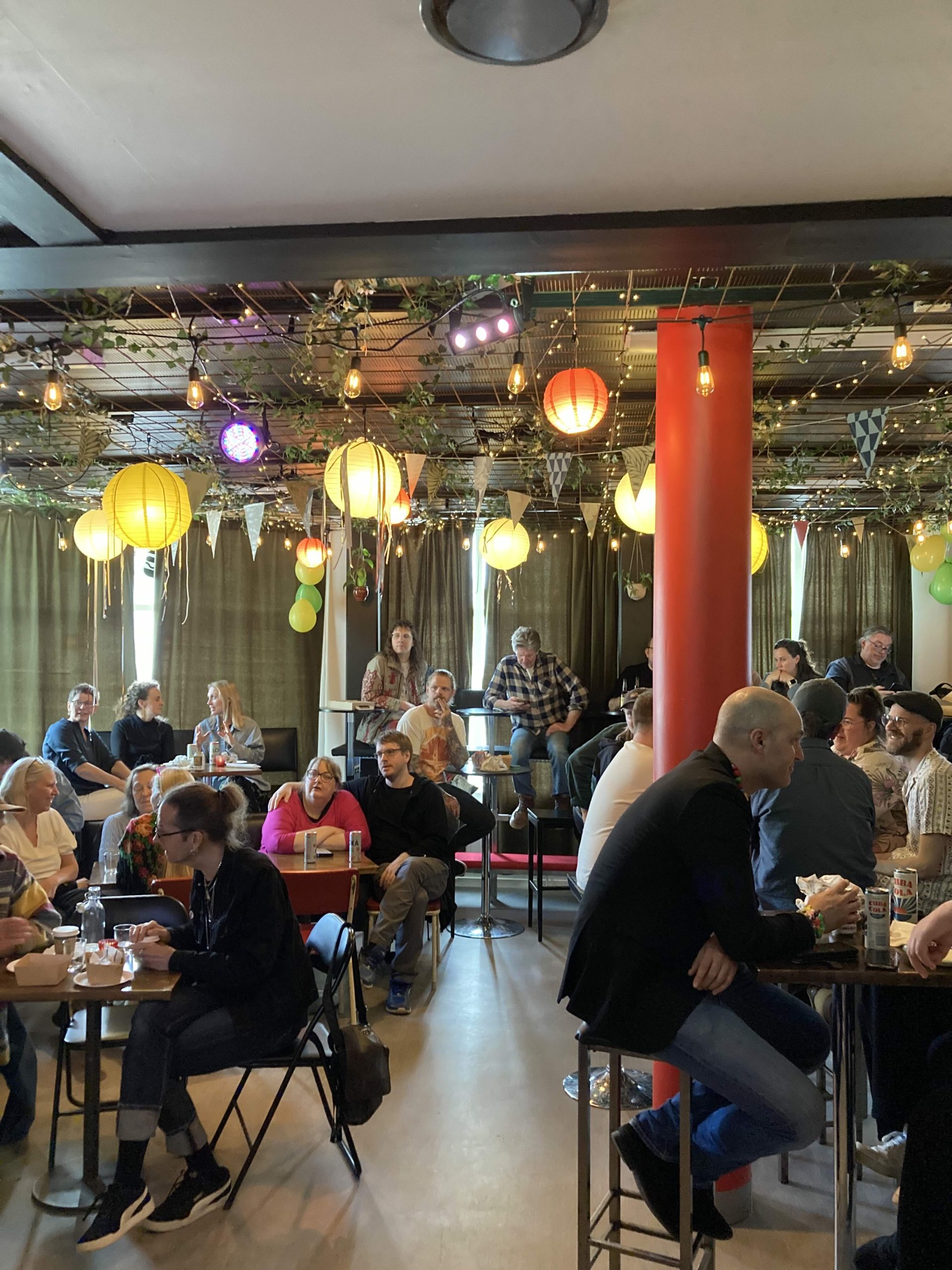 En välbefolkad lokal. Kulörta lyktor och ballonger och girlanger i taket.