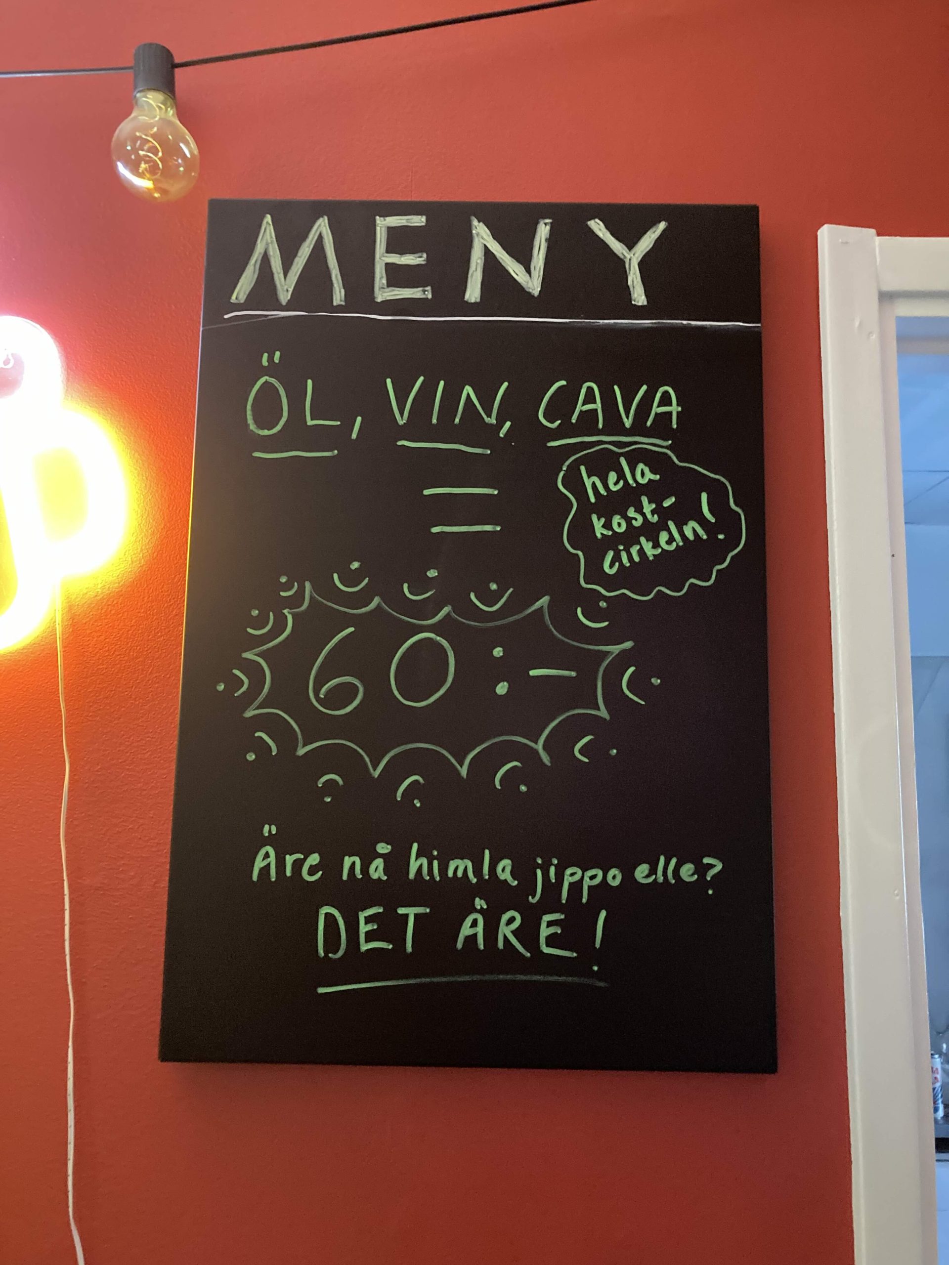 En svart skylt med texten "MENY: Öl, vin, cava = 60 kr" "Hela kostcirkeln"