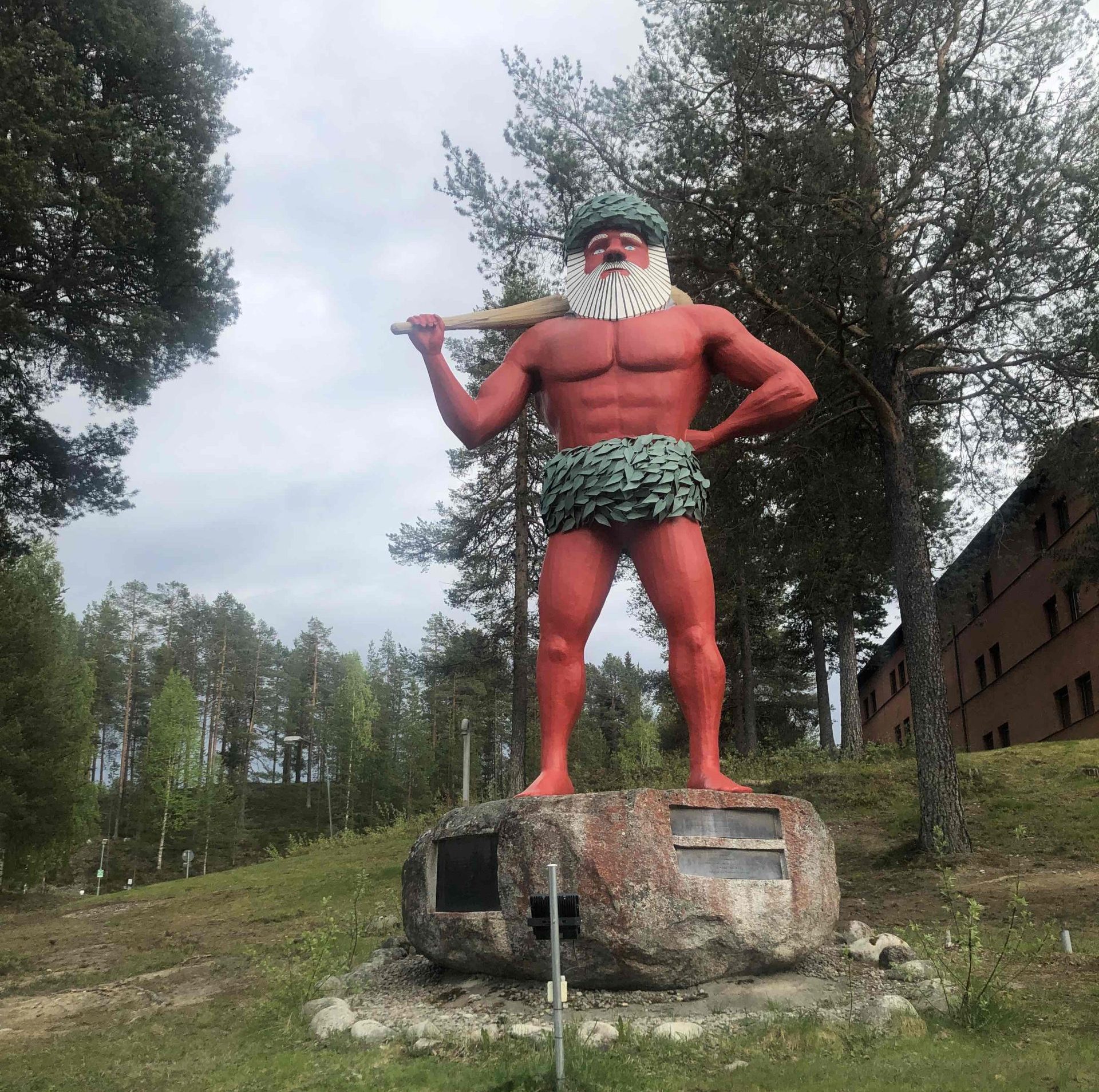 En hög staty föreställande en muskulös man med illröd hud, stort vitt skägg, en kjol och krans av gröna löv. Han står bredbent med ena handen i sidan, och andra handen håller om en stor träpåk som vilar över axeln. Mannen har uppspärrade ögon och blickar ut i intet.