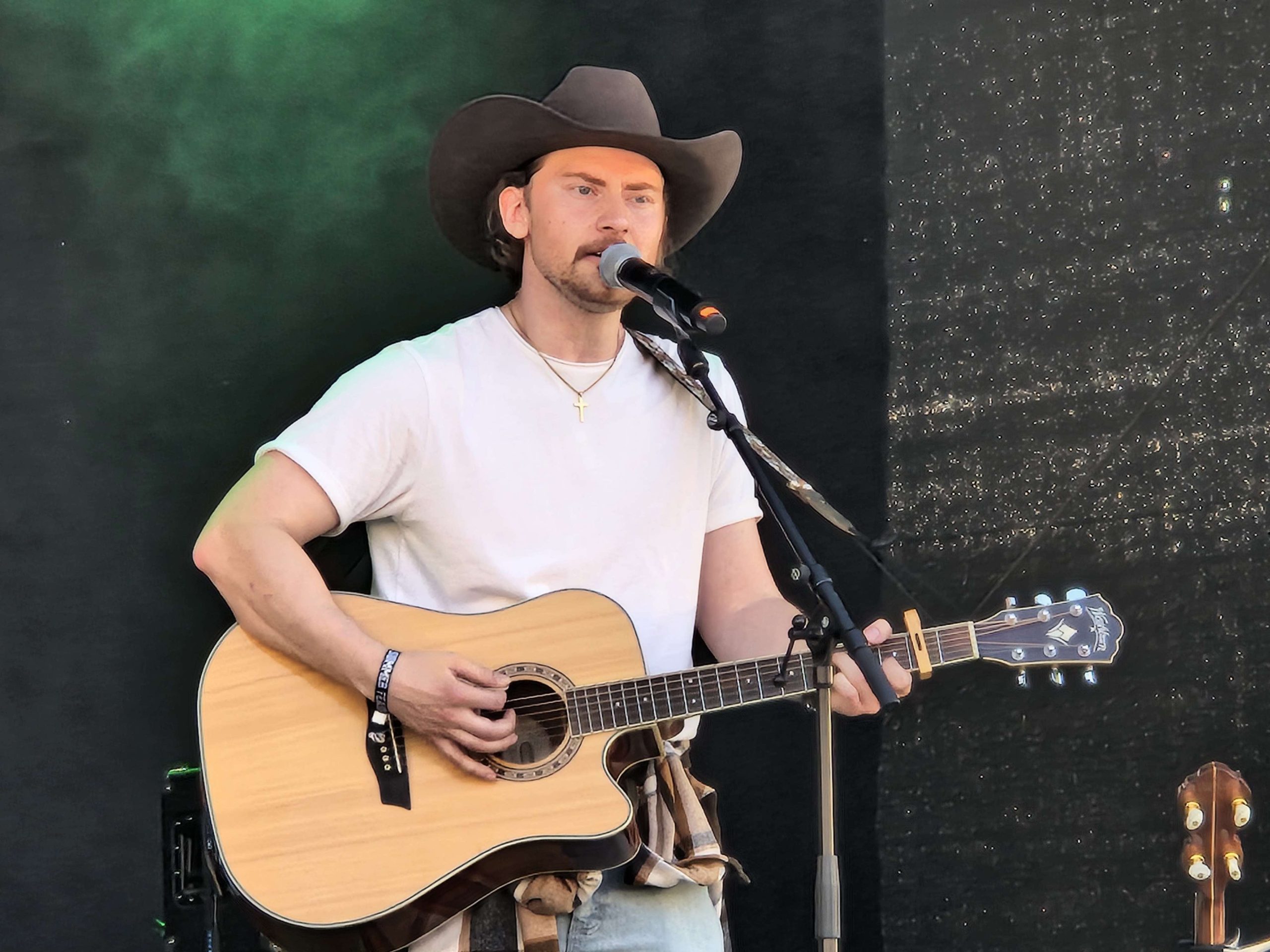 En kille med gitarr som spelar gitarr och ser ut på publiken framför scenen. Han har cowboyhatt, vit t-shirt och blåjeans.