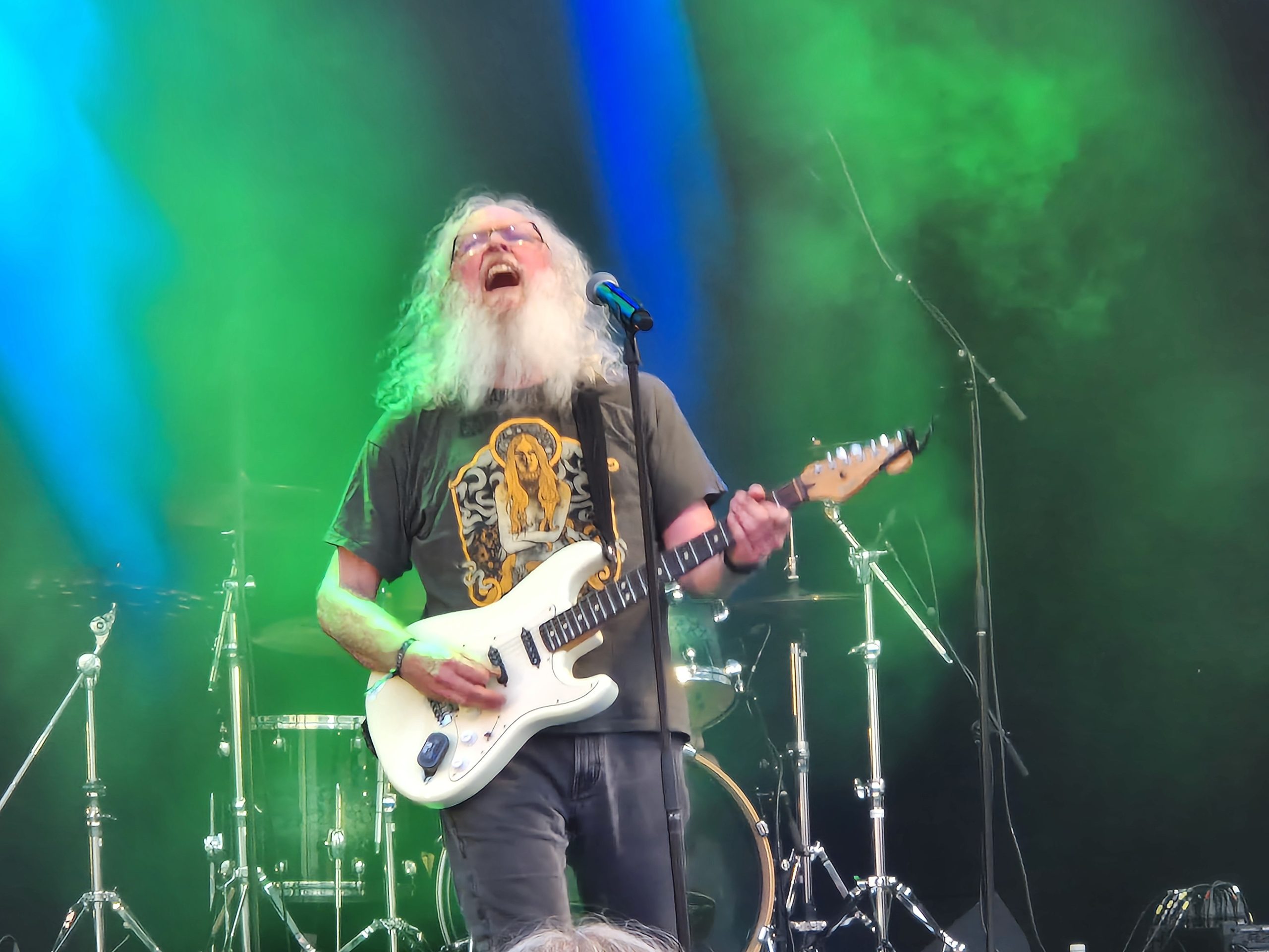 Gitarristen skriker och spelar på sin vita elgitarr. Han har långt, vitt hår och skägg.