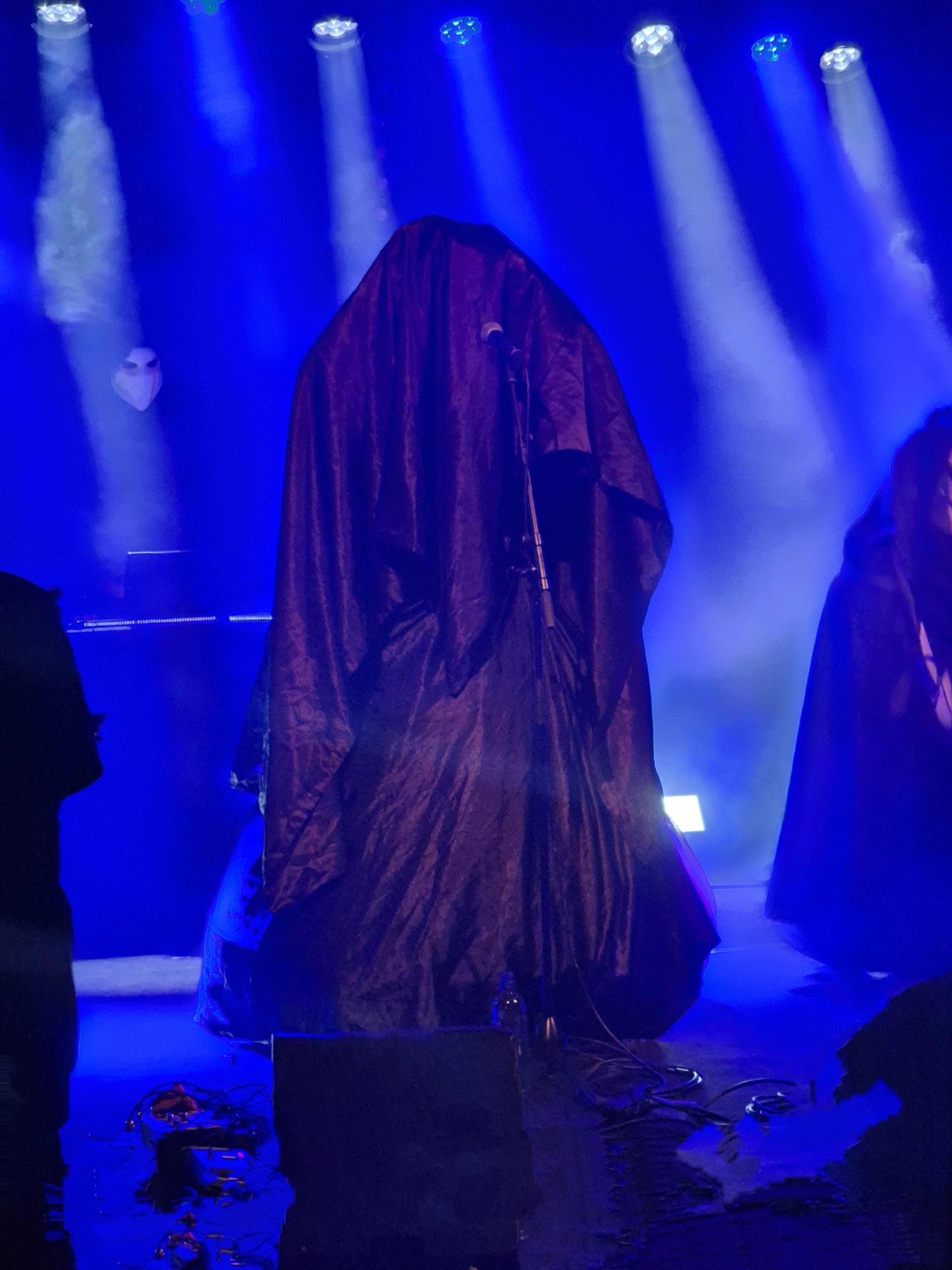 Bandet Blackworns sångare, insvept i ett stort, svart tyg, som mest ser ut som en stor hög med tyg. Hon sjunger genom tyget i en mikrofon. Scenen är rökig och har blått scenljus.