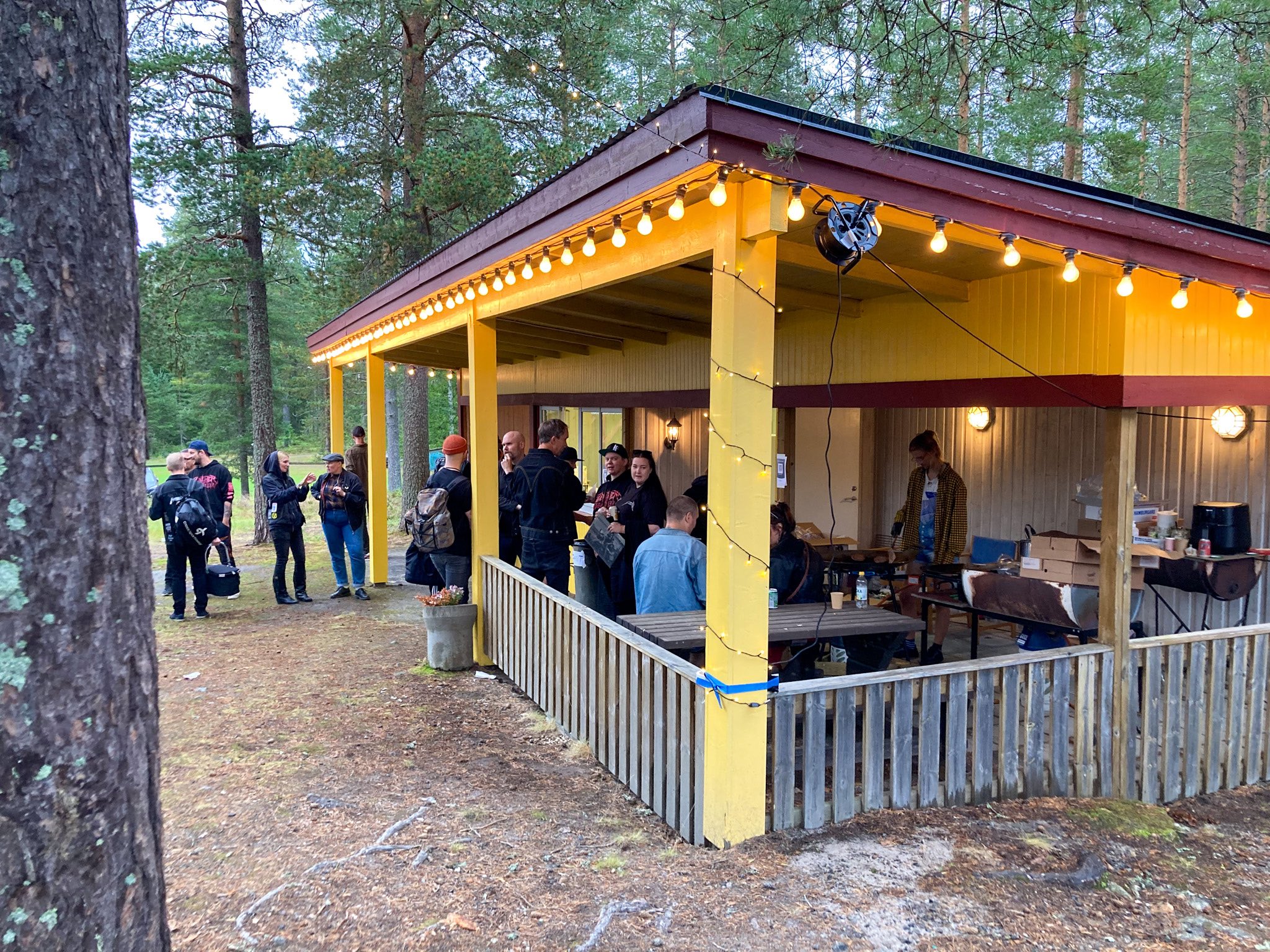 Kiosken är en liten byggnad i trä med en liten kioskkur, bänkar och staket. Flera människor står under taket.