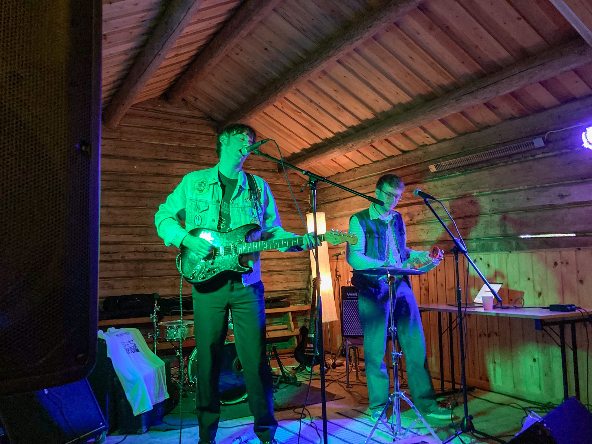 Två killar på scenen i logen. Den ena är lång, har jeansjacka och sjunger i mikrofonen medan han spelar elgitarr. Bredvid honom står en kortare kille med jeansväst och glasögon och spelar tamburin.