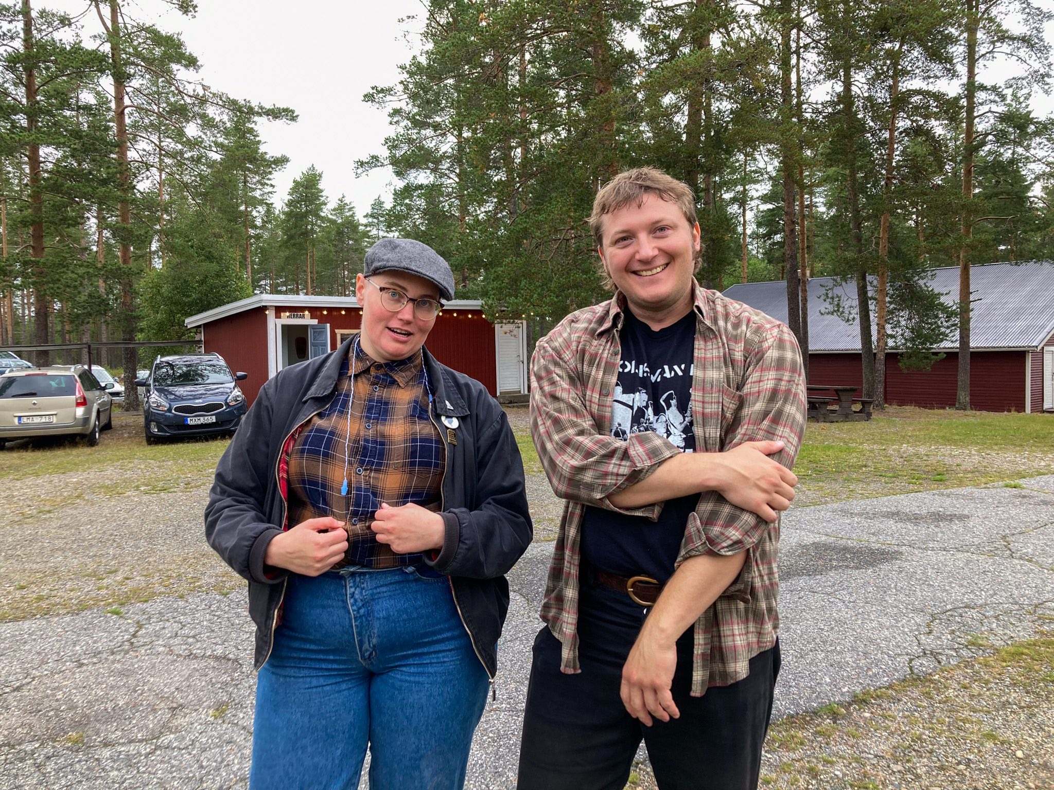 En kvinna och en man står bredvid varandra och ler mot kameran. Båda har rutiga skjortor. Kvinnan har basker och blå jeans. Mannen har en bandtröja och svarta jeans. De är i 30-årsåldern.
