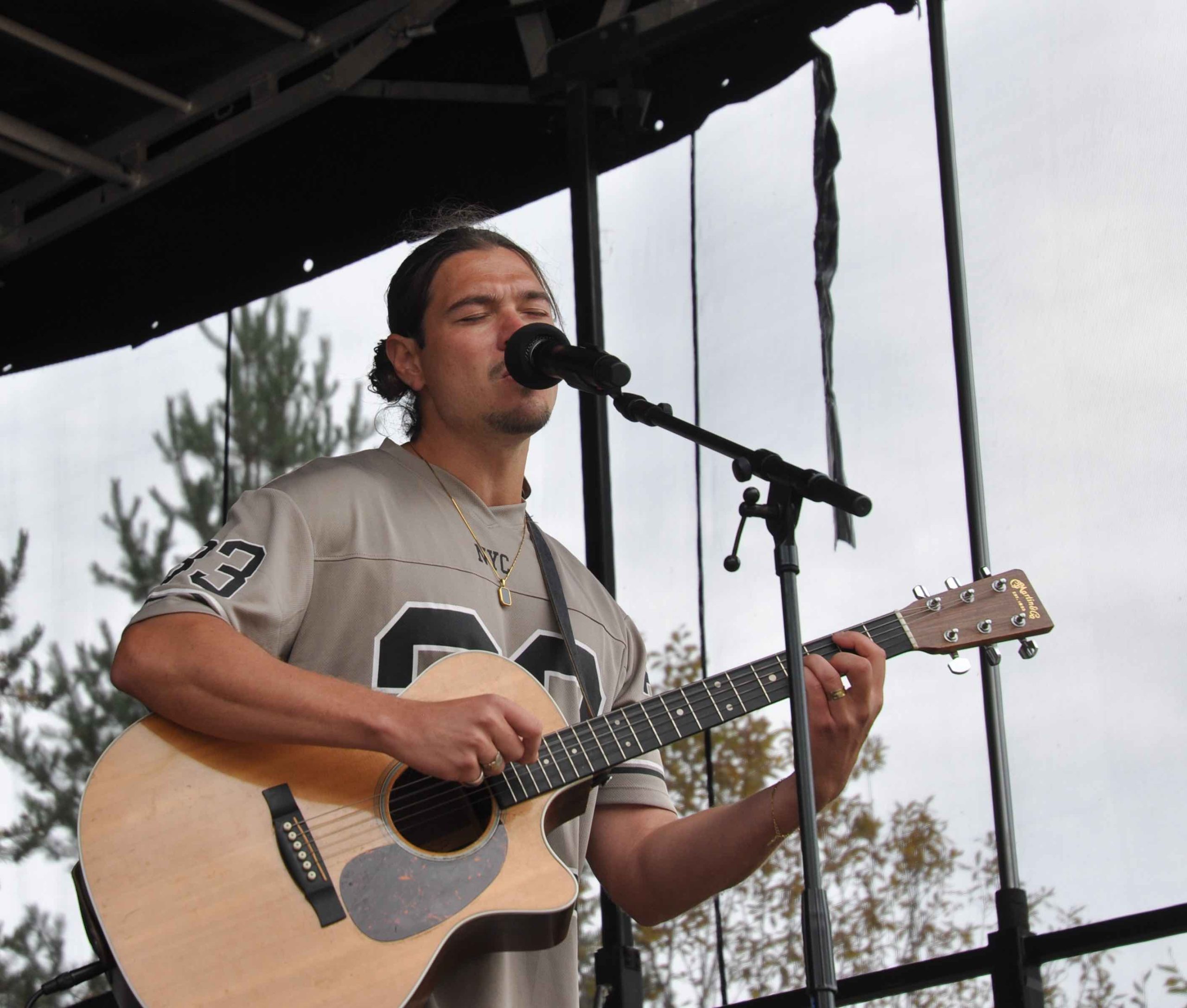 Josef Love på scen. Han sjunger med slutna ögon medan han spelar gitarr. Han har en grå sportig t-shirt och mörkt hår uppsatt i en knut.