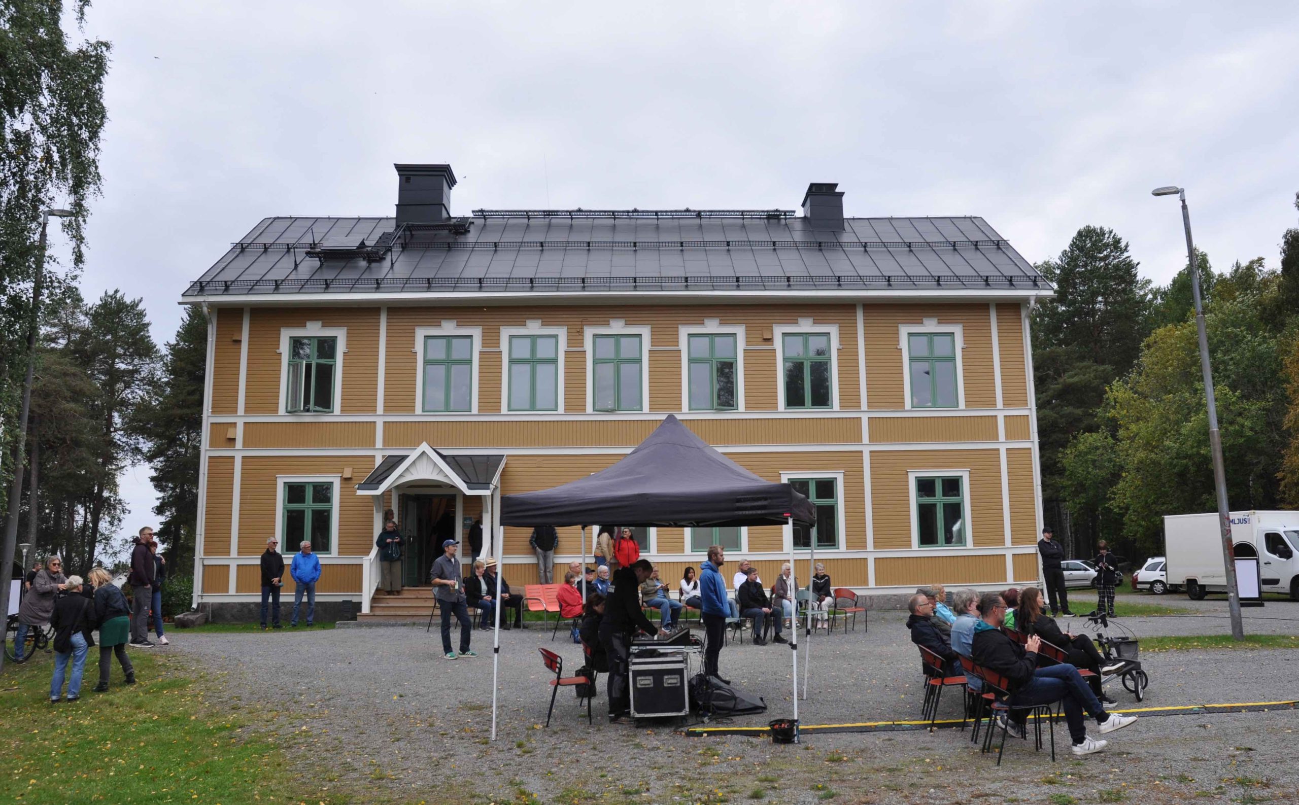 På baksidan av Blackis står ett litet tält uppställt där en ljudtekniker står under med sitt mixerbord. Framför tältet står stolar framställda där det sitter några personer.