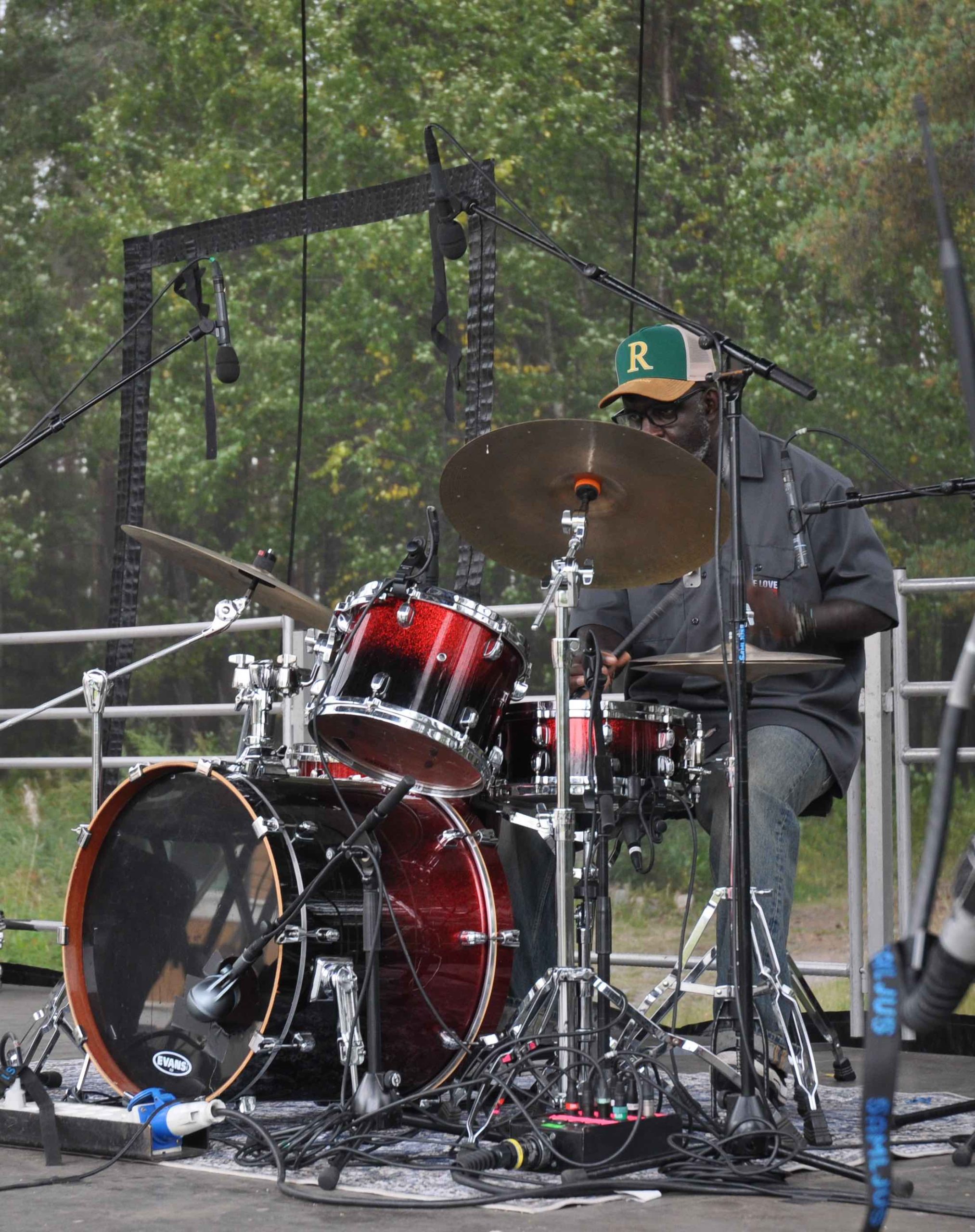 Trummisen i Josef Loves band. Han har keps, jeans och en grå, kortärmad skjorta.