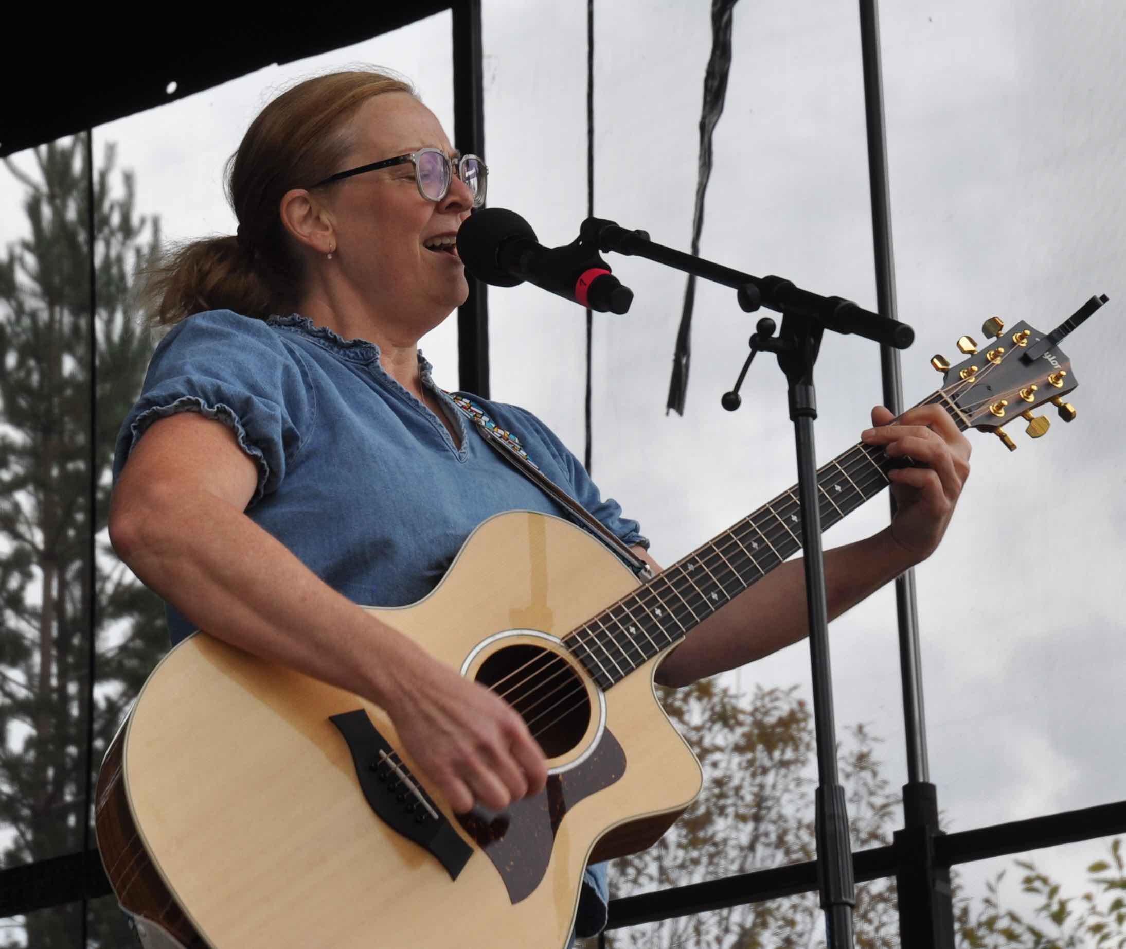 Artisten Anna Sellén står på scenen och sjunger i en mikrofon på stativ medan hon spelar på en akustisk gitarr. Hennes ögon är slutna.