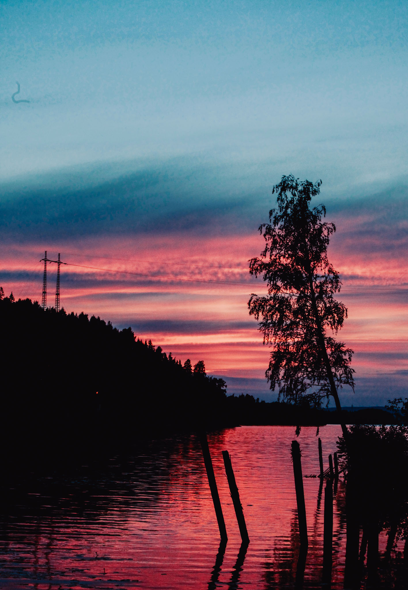En solnedgång vid en sjö. Himlen är randigt rosa och blå och speglar sig i vattnet.
