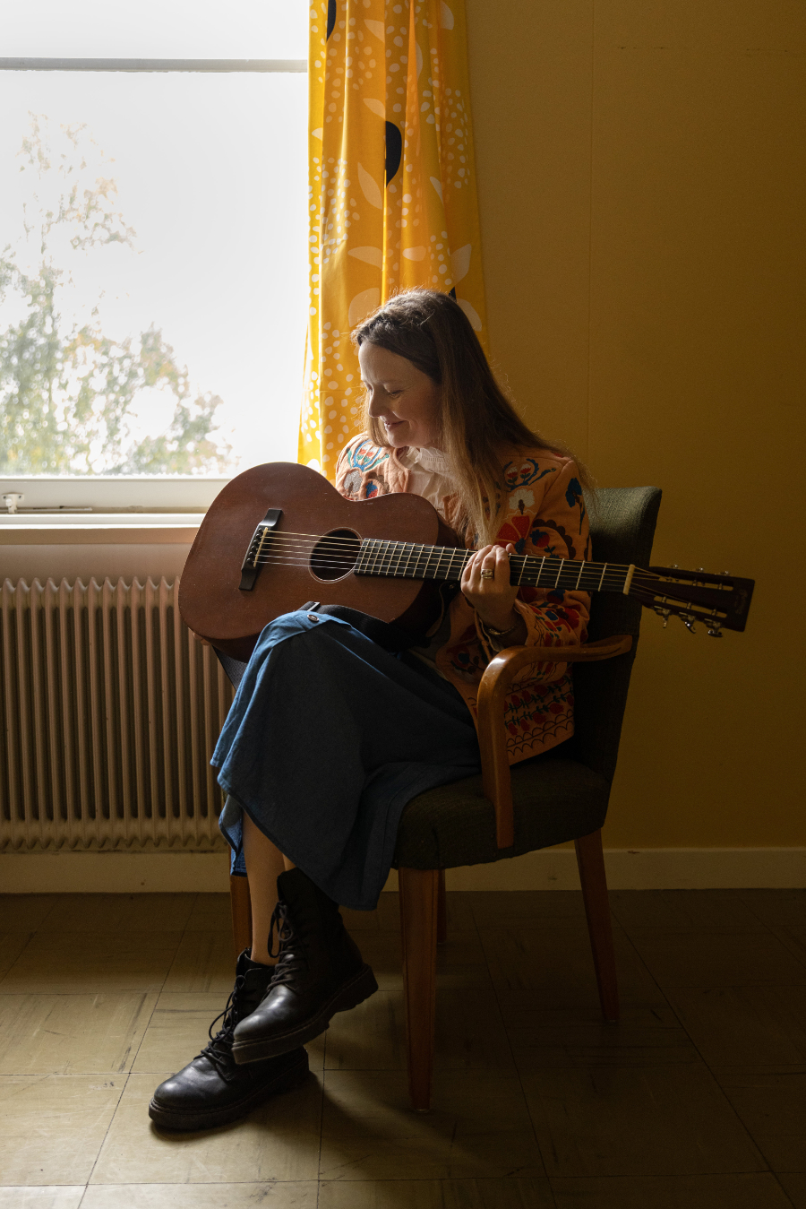Ellen Sundberg sitter på en gammal stol och håller i en gitarr.