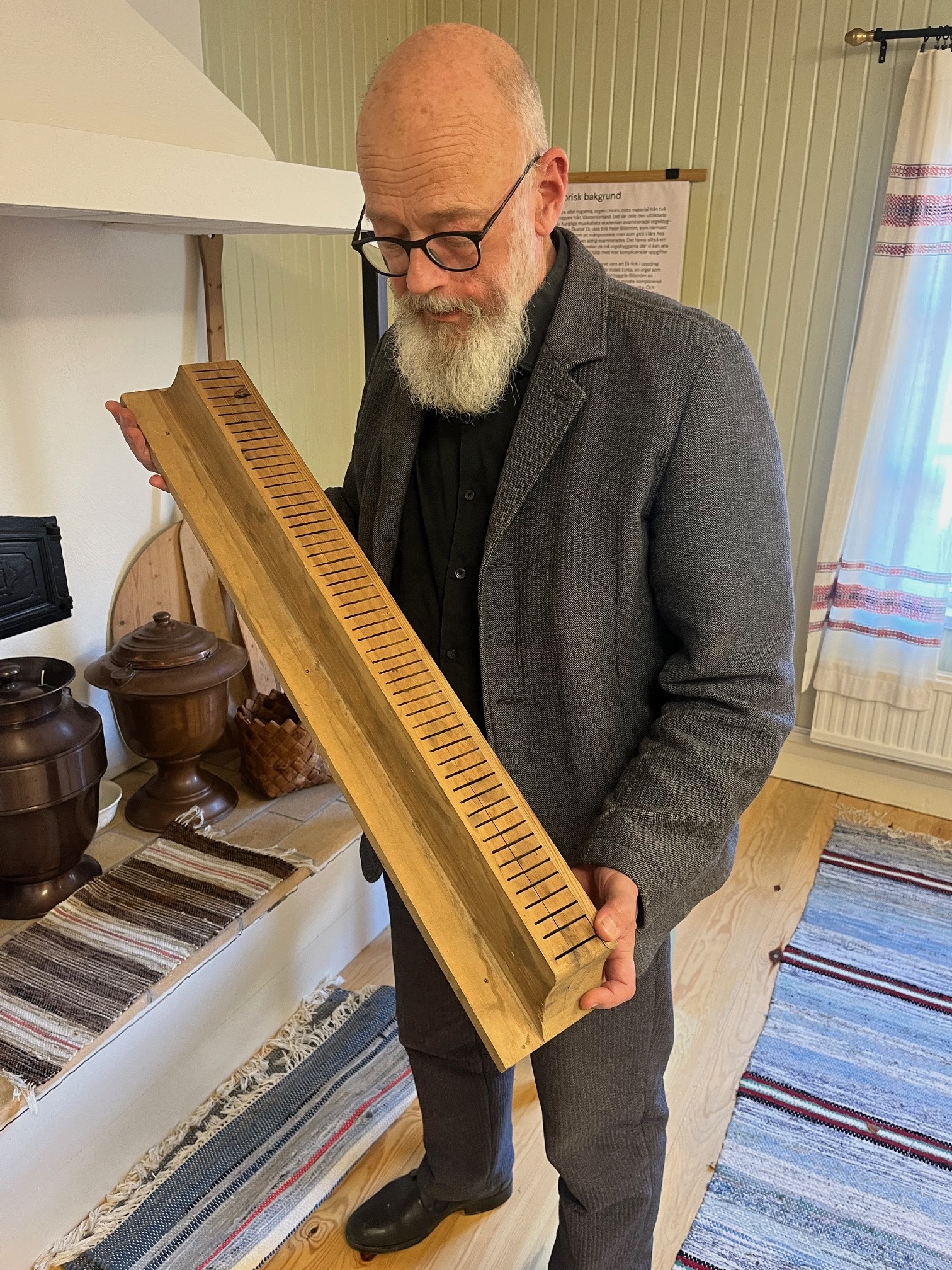 Hans-Ola står och håller en massiv bit trä som troligtvis är en del av den gamla orgeln. Han står i utställningslokalen.