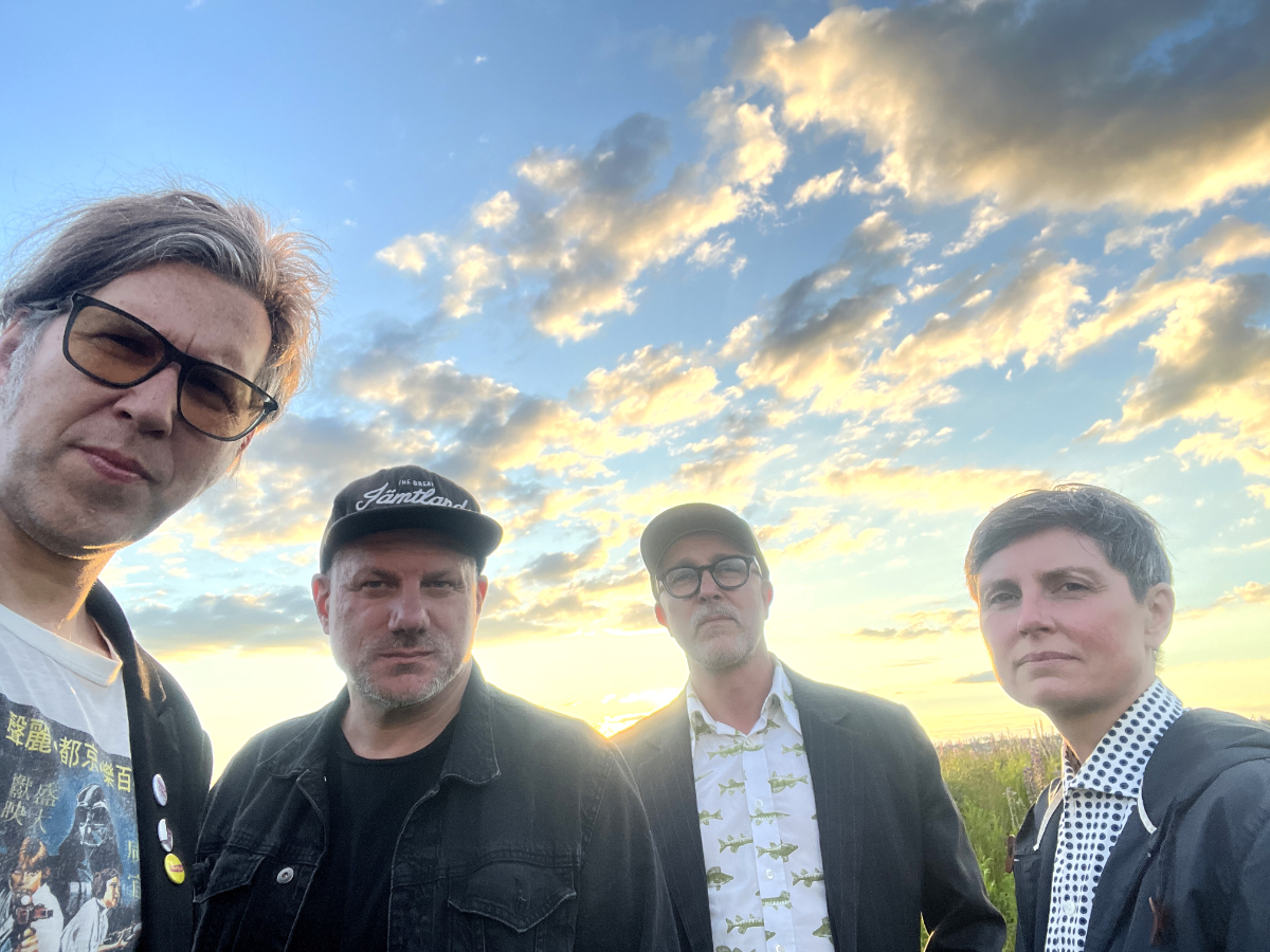 De fyra medlemmarna i The Confusions står utomhus med en molnig himmel i bakgrunden.